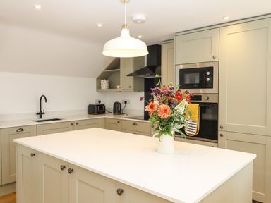 A kitchen with a central island topped with flowers a black sink and faucet ovens and a microwave at Bumblebee Cottage in East Nynehead near Bradford-On-Tone