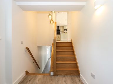 A wooden staircase leading up to a kitchen with white walls and hanging lights at Bumblebee Cottage in East Nynehead near Bradford-On-Tone