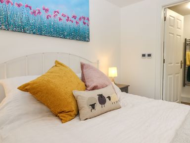 A bedroom with a white bed and three decorative pillows a bedside table with a lamp and a painting of pink flowers at Bumblebee Cottage in East Nynehead near Bradford-On-Tone