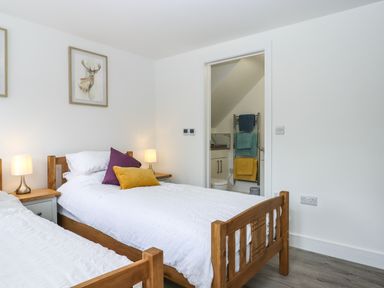 A bedroom with two wooden single beds white bedding purple and yellow pillows bedside tables with lamps and a doorway leading to a bathroom at Bumblebee Cottage in East Nynehead near Bradford-On-Tone