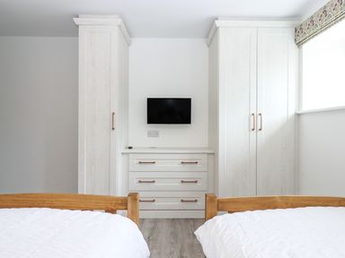 A bedroom with two wooden beds white bedding white wardrobes and a small wall mounted television at Bumblebee Cottage in East Nynehead near Bradford-On-Tone