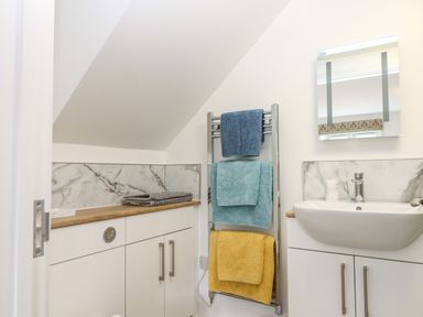 A bathroom with a sink mirror towels on a heated rack and marble backsplash at Bumblebee Cottage in East Nynehead near Bradford-On-Tone
