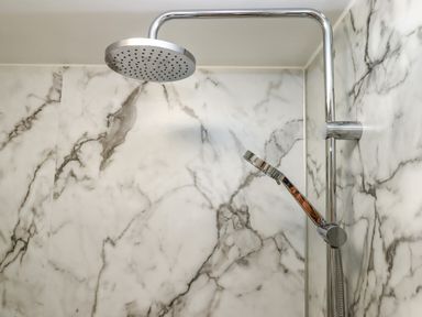 A shower head and handheld shower on a rail against a marble wall