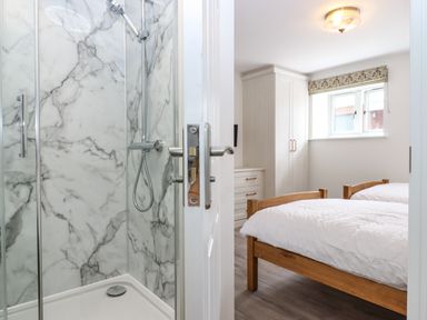 A bathroom with a marble shower next to a bedroom with two beds and a wardrobe at Bumblebee Cottage East Nynehead near Bradford-On-Tone