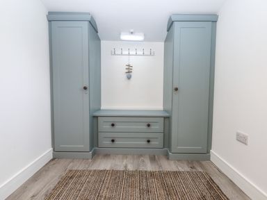 A hallway with two tall cabinets and a chest of drawers between them with hooks above on the wall at Bumblebee Cottage in East Nynehead near Bradford-On-Tone