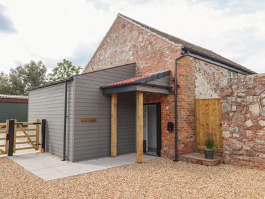 An exterior view of a brick and wood panel building with a gated entrance and a small covered porch at Bumblebee Cottage in East Nynehead near Bradford-On-Tone