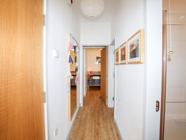 A hallway with wooden floor leading to a bedroom with a bed and nightstands at Gwel Y Mor in Pwllheli