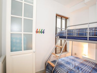 A bunk bed with plaid bedding in a room with a window and a door at Gwel Y Mor in Pwllheli
