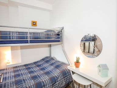 A bedroom with a bunk bed featuring blue plaid bedding a small white desk with a cactus a small house model and a round mirror on the wall at Gwel Y Mor in Pwllheli