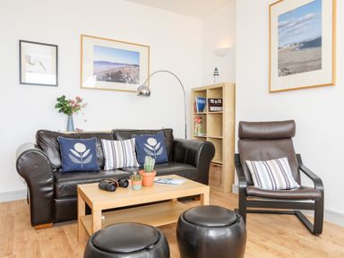 A living room with a black leather sofa and chair a wooden coffee table and framed pictures on the walls at Gwel Y Mor in Pwllheli