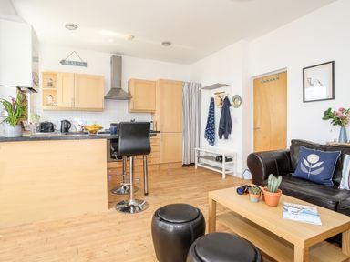 A kitchen and living area with wooden cabinets black stools a leather sofa and a wooden coffee table at Gwel Y Mor in Pwllheli