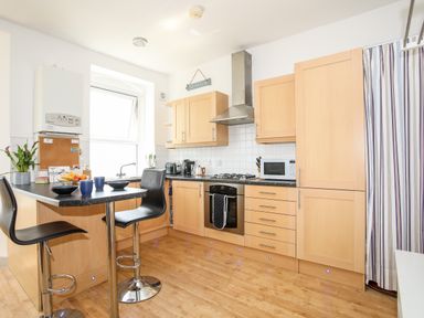 A kitchen with wooden cabinets black countertop and stools at Gwel Y Mor in Pwllheli