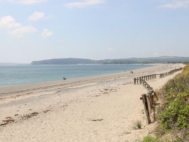A sandy beach with a wooden fence and a few people near the water at Gwel Y Mor in Pwllheli
