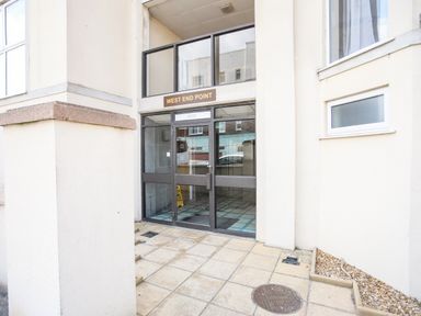The entrance door to a building with a sign above reading West End Point surrounded by tiled pavement and windows at Gwel Y Mor in Pwllheli