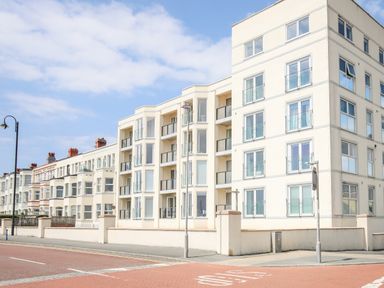 A street view of a modern white apartment building with balconies and large windows
