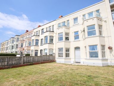 Exterior view of a row of multi-story residential buildings with bay windows and fenced yards at Gwel Y Mor in Pwllheli