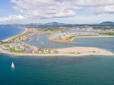 An aerial view of a coastal town with a marina boats and houses near a beach at Gwel Y Mor in Pwllheli