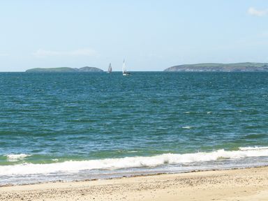 A sandy beach with waves and sailboats on the sea at Gwel Y Mor in Pwllheli