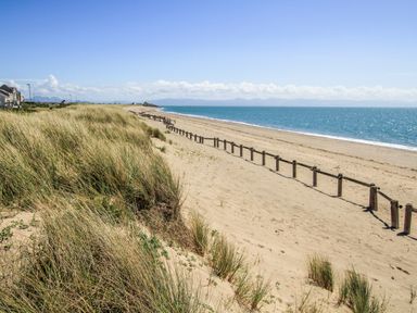 A sandy beach with grassy dunes and wooden posts along the shore at Gwel Y Mor in Pwllheli