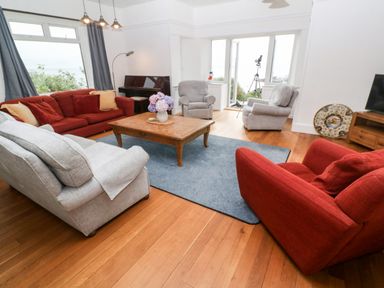 A living room with red and grey sofas a wooden coffee table with flowers and a telescope by open doors at Penmarth House in Coverack