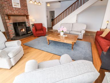A living room with armchairs sofas a wooden coffee table a rug and a brick fireplace at Penmarth House in Coverack
