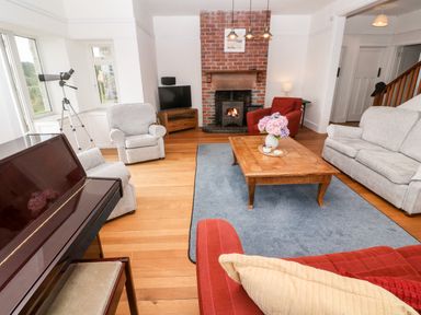 A living room with a piano a fireplace armchairs a sofa a wooden coffee table with flowers and a blue rug at Penmarth House in Coverack