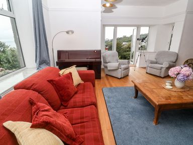 A living room with a red sofa gray armchairs a wooden coffee table a piano and a telescope at Penmarth House in Coverack