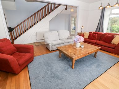 A living room with a wooden coffee table and flowers on a rug with sofas and armchair at Penmarth House in Coverack