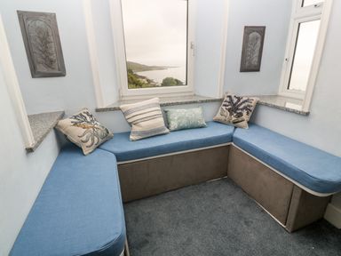 A corner seating area with blue cushions and decorative pillows by windows showing a coastal view at Penmarth House Coverack