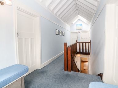 A carpeted hallway with wooden stair railing and white paneled doors at Penmarth House in Coverack
