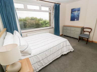 A bedroom with a bed bedside table lamp dresser chair large window with curtains at Penmarth House in Coverack