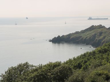 A coastal view with rocky cliffs green trees and several boats on the water at Penmarth House in Coverack