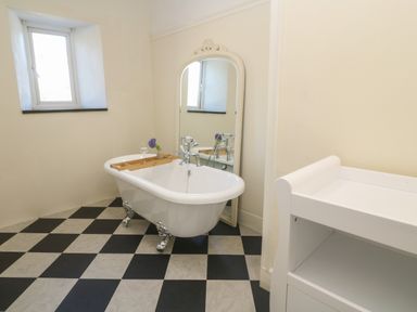 A bathroom with a clawfoot bathtub a large mirror a small window and a white changing table at Penmarth House in Coverack