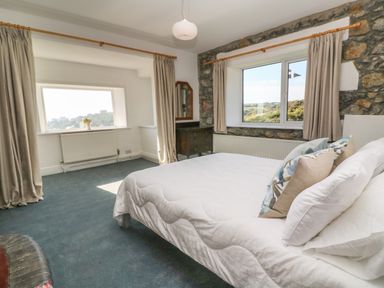 A bedroom with a bed pillows windows with curtains a dresser and stone walls at Penmarth House in Coverack