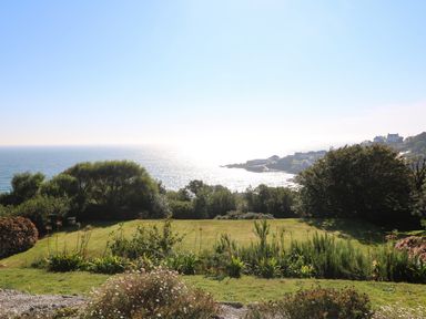 A garden with grass and bushes overlooking the sea and a coastal village at Penmarth House in Coverack