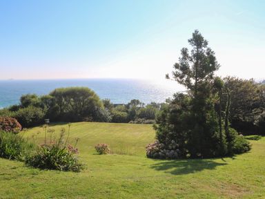 A grassy garden with trees and bushes overlooking the ocean at Penmarth House in Coverack