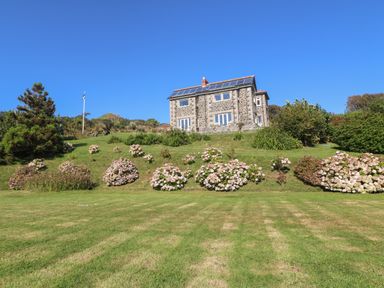 A stone house with solar panels on the roof surrounded by grass and flowering bushes at Penmarth House in Coverack