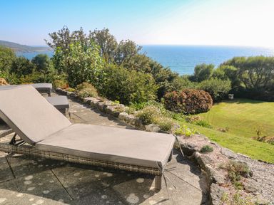 A patio with outdoor lounge chairs overlooking a garden and the sea at Penmarth House in Coverack