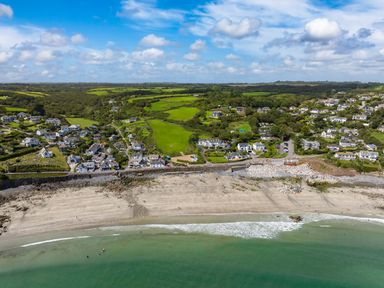 A beach with people near the water and a village with houses and green fields behind it at Penmarth House in Coverack