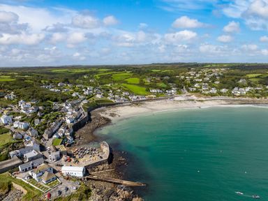 An aerial view of a coastal village with houses green fields a beach a small harbor with boats and calm water at Penmarth House in Coverack