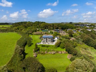A stone house with solar panels on the roof surrounded by grass, shrubs, trees and a flagpole at Penmarth House in Coverack