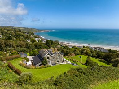 A house with a large lawn and flagpole near a coastline with a beach and ocean at Penmarth House Coverack