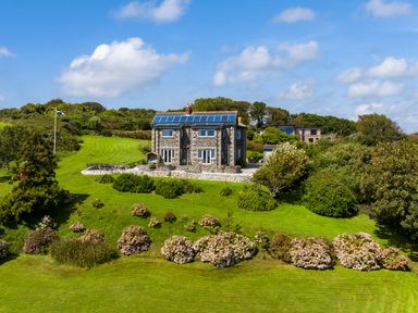 A stone house with solar panels on the roof surrounded by green lawn and bushes at Penmarth House in Coverack