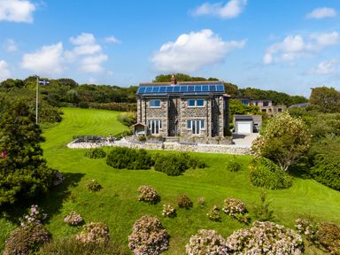 A stone house with solar panels on the roof surrounded by garden and greenery at Penmarth House in Coverack