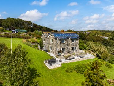 A stone house with solar panels on the roof surrounded by a large lawn and outdoor seating areas at Penmarth House in Coverack