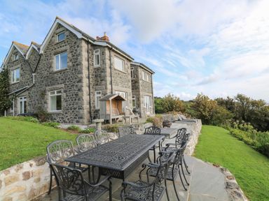 An outdoor patio area with a black metal dining table and chairs next to a stone house at Penmarth House in Coverack