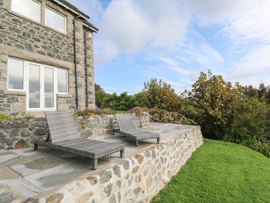 An outdoor stone patio with two lounge chairs next to a stone house and a garden at Penmarth House in Coverack
