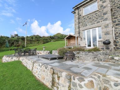 A stone patio with outdoor dining set lounge chair fire pit and barbecue beside a stone house at Penmarth House in Coverack