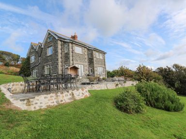 A stone house with a patio and outdoor dining set in a grassy garden at Penmarth House in Coverack