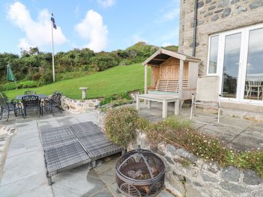 An outdoor patio area with black metal table and chairs wooden bench with roof and glass doors at Penmarth House in Coverack